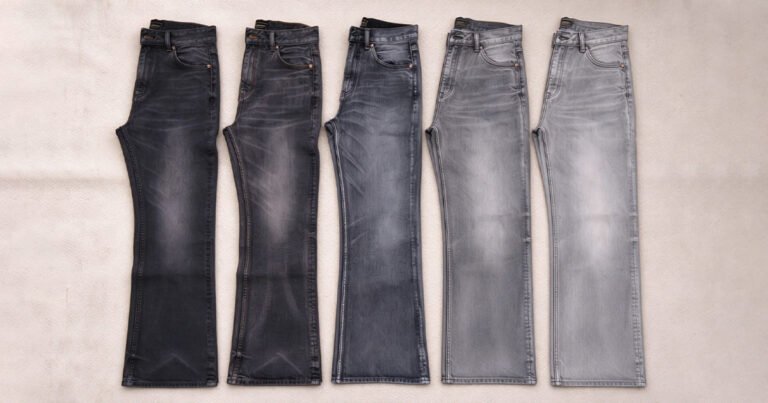 Top-down flat lay shot of five pairs of jeans arranged left to right from deep black to pale grey, showcasing a spectrum of fading wash results for black denim